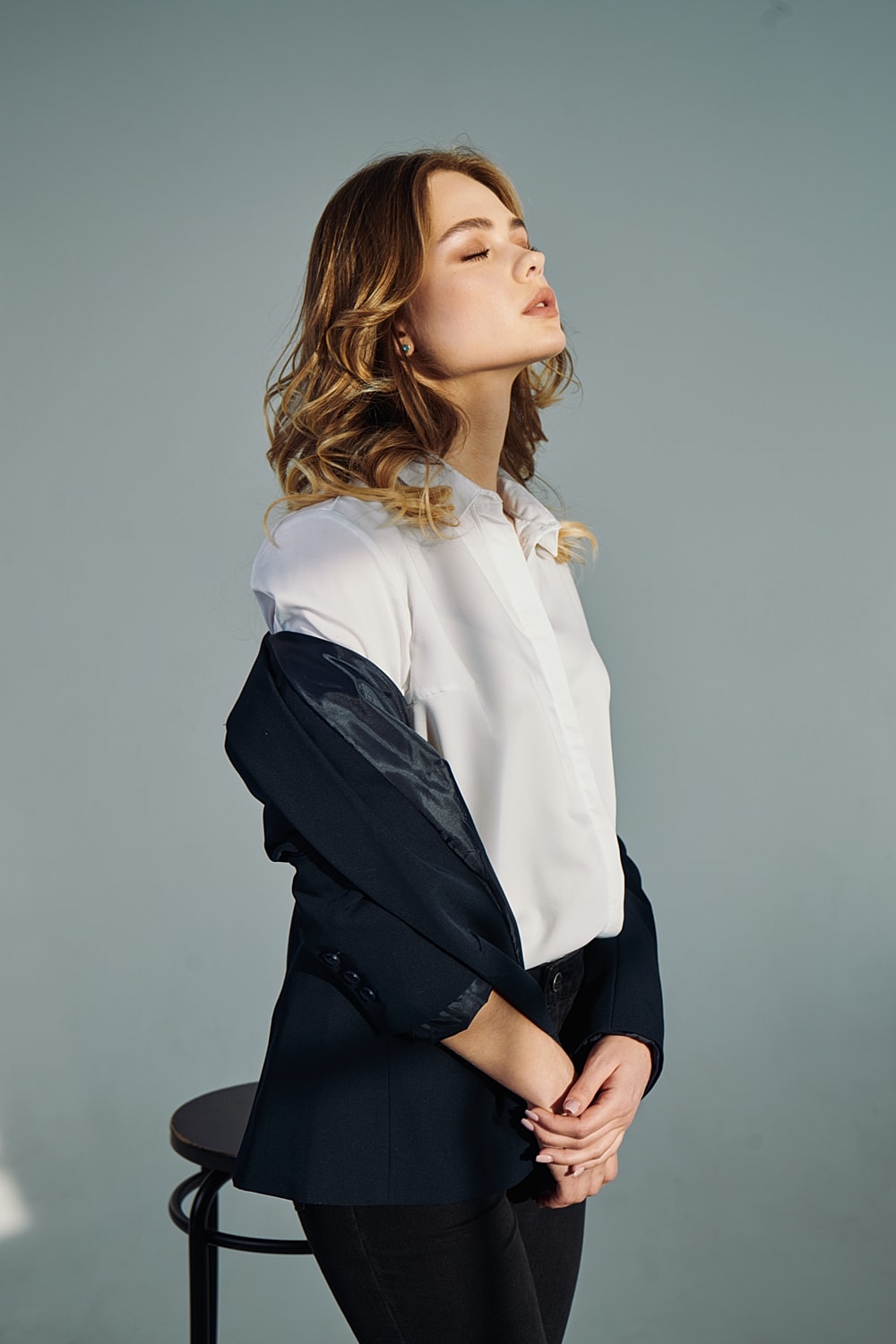 Woman in stylish attire, serene expression, neutral background.