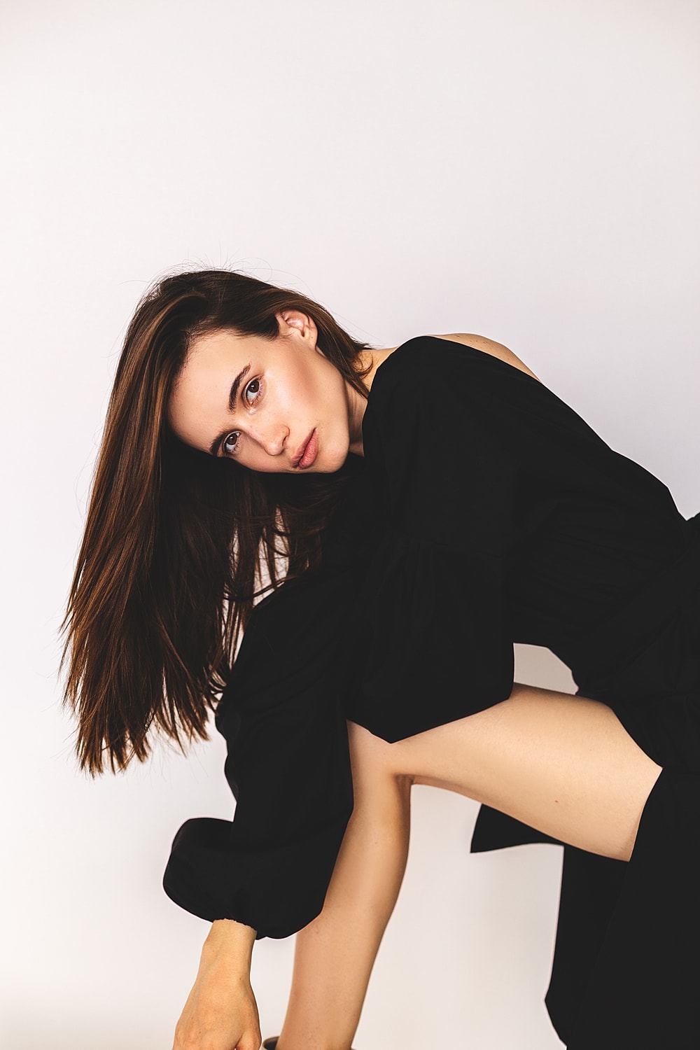 Woman in black dress posing creatively against white background.