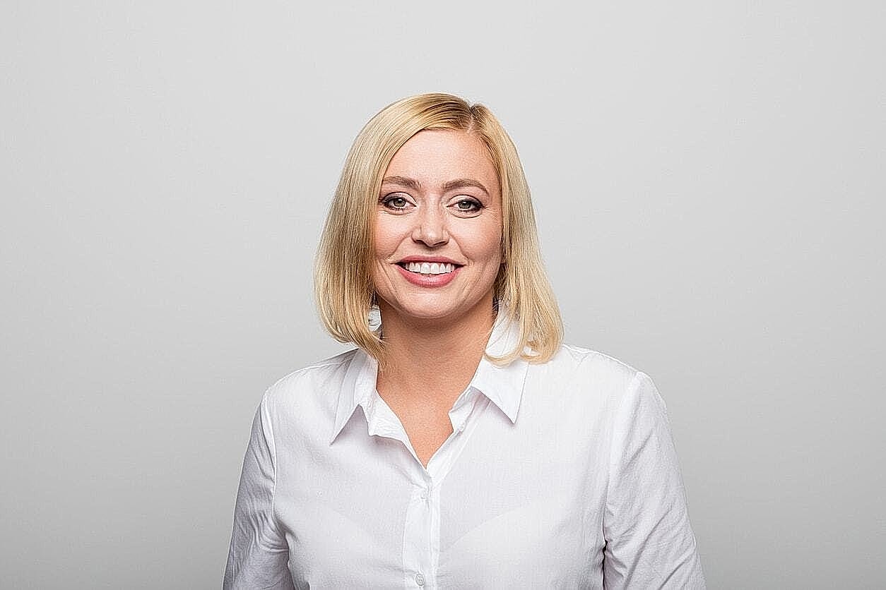Smiling woman in a white shirt, plain background.