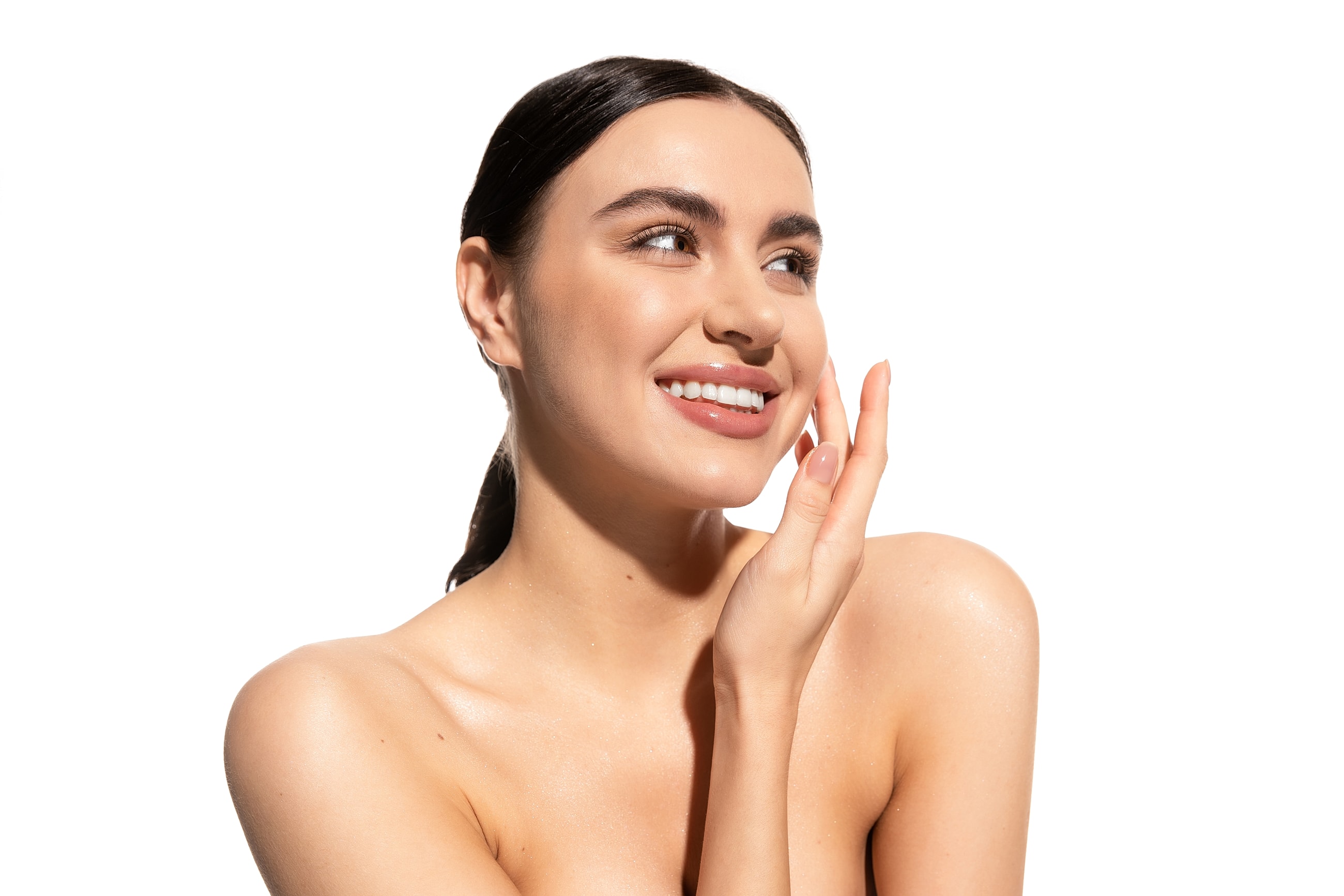 Smiling woman with glowing skin, touching face.